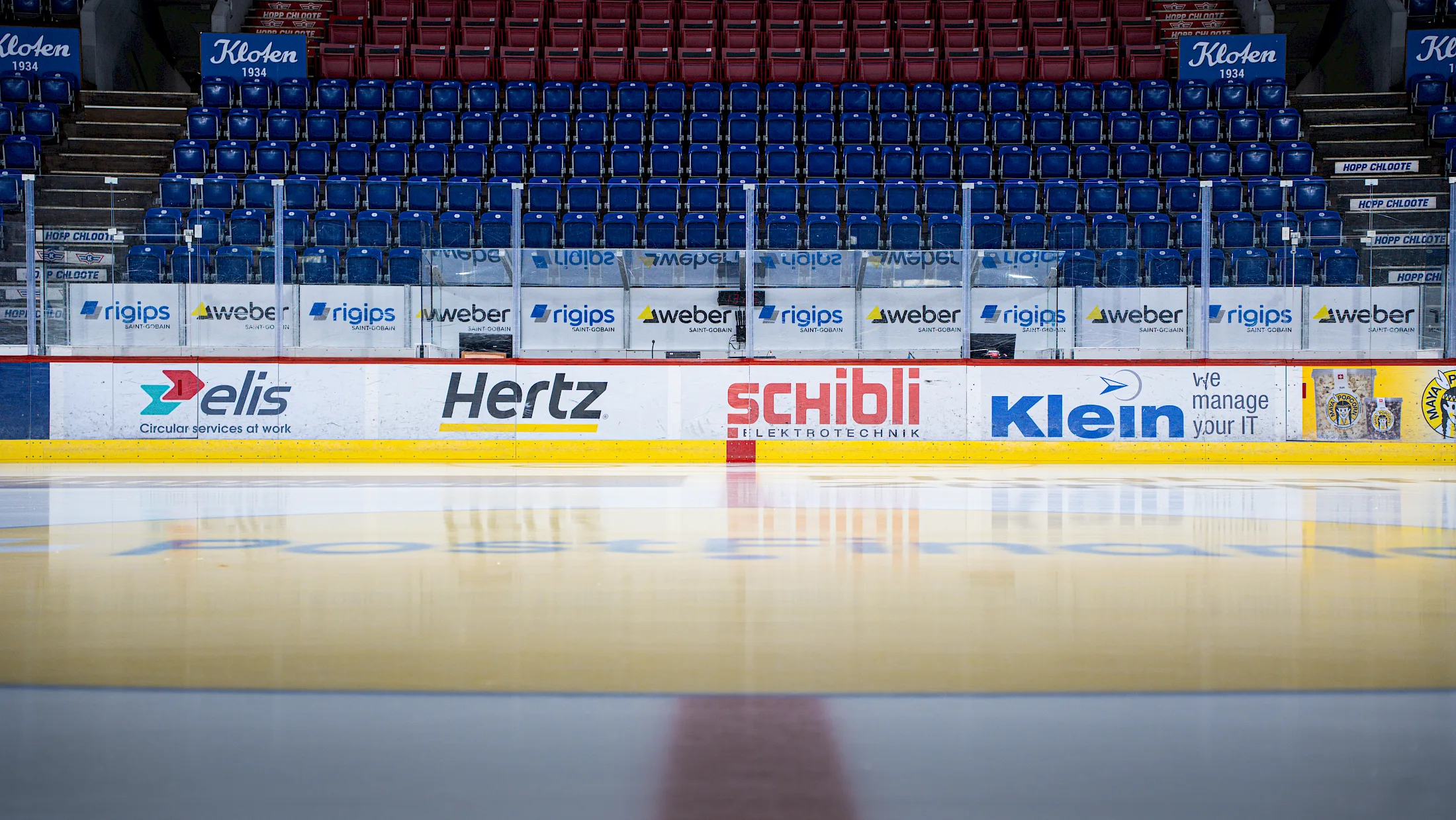 Leere Zuschauertrib&uuml;ne und Bande mit Sponsorenlogos wie Hertz, Schibli und Klein hinter der Eisfl&auml;che