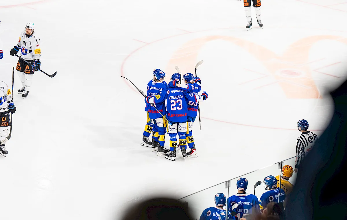 Spieler in blauem Kloten-Trikot mit Puck am Schl&auml;ger, umgeben von Gegnern in weissen Trikots