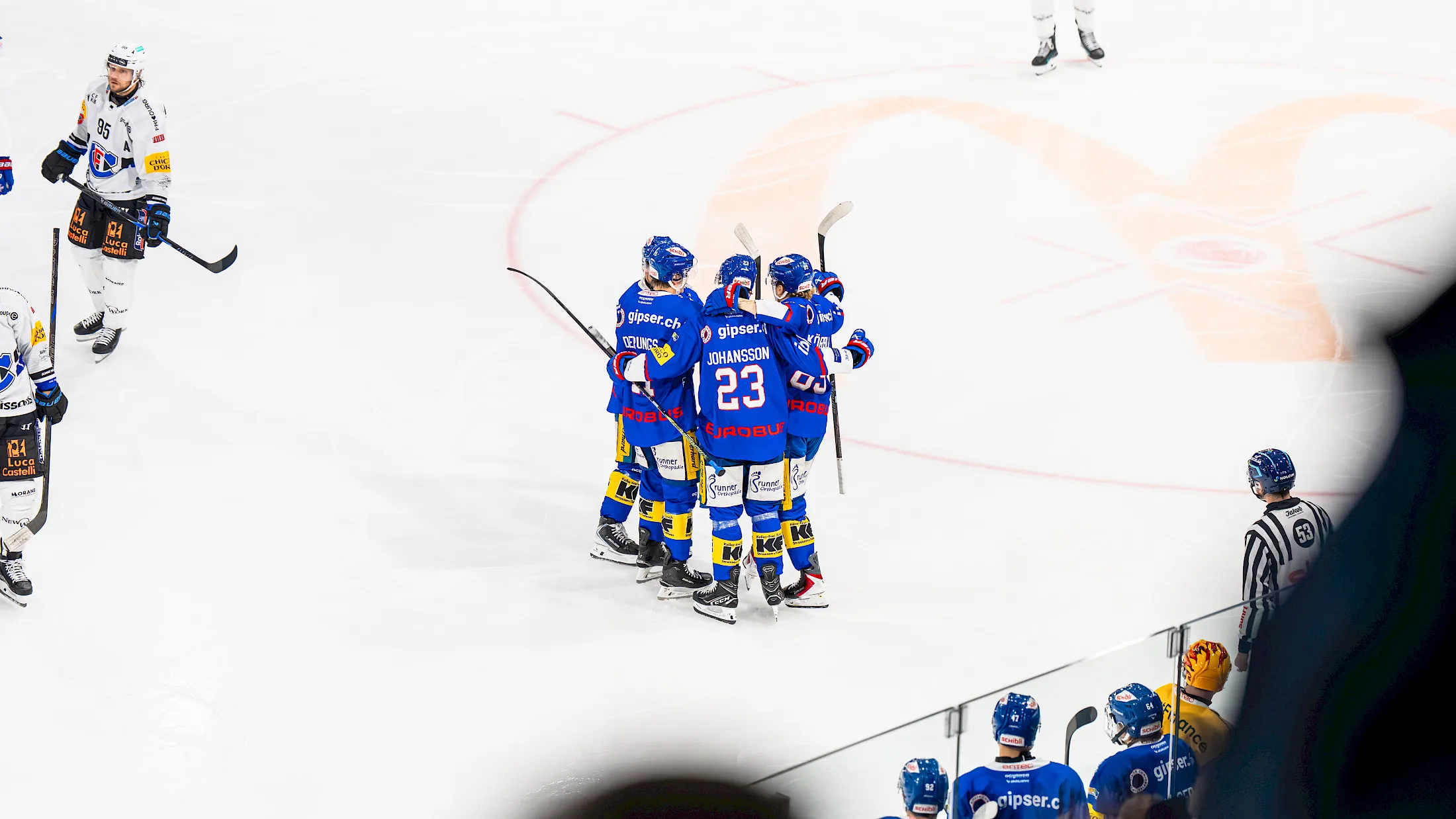 Spieler in blauem Kloten-Trikot mit Puck am Schl&auml;ger, umgeben von Gegnern in weissen Trikots