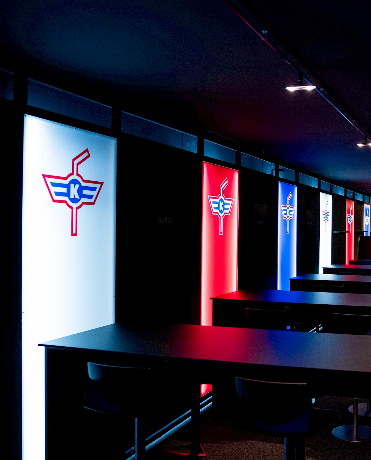 Beleuchtete Logo-Panels des EHC Kloten in einer Lounge mit Tischreihen und Sitzpl&auml;tzen