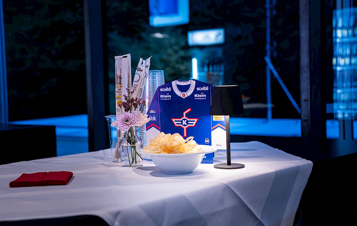 Getr&auml;nkekarte im Trikot-Design mit Snacks und Blumen auf einem Tisch, im Hintergrund G&auml;ste